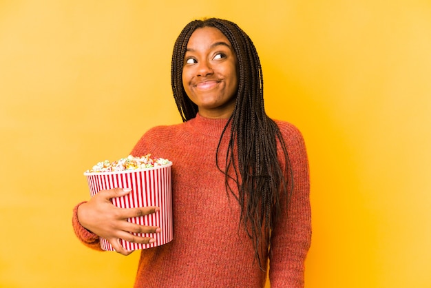 Jeune femme afro-américaine tenant un pop-corn isolé rêvant d'atteindre les objectifs et les buts