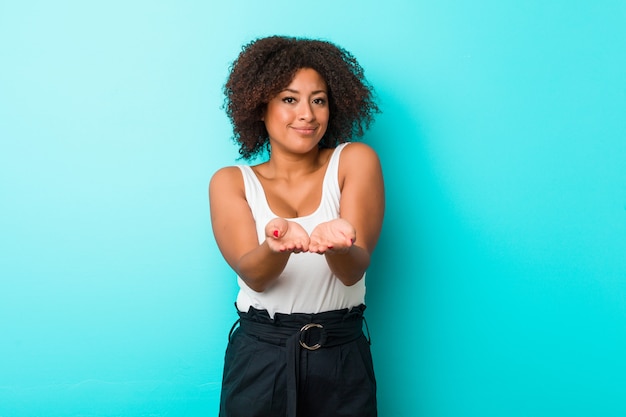 Jeune femme afro-américaine tenant quelque chose avec des paumes, offrant à la caméra.