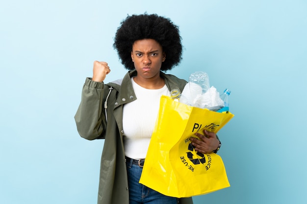 Jeune femme afro-américaine tenant un sac de recyclage isolé sur coloré avec une expression malheureuse