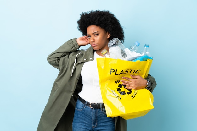 Jeune femme afro-américaine tenant un sac de recyclage isolé sur un mur coloré ayant des doutes