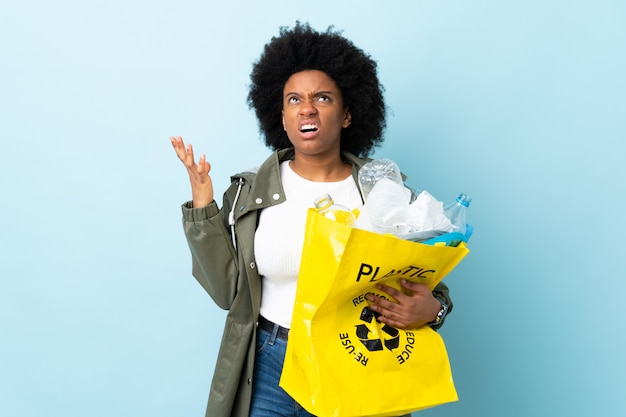 Jeune femme afro-américaine tenant un sac de recyclage sur un mur coloré souligné accablé