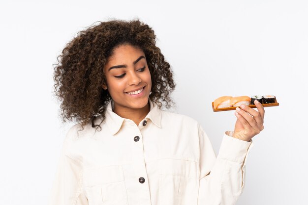 Jeune femme afro-américaine tenant des sushis isolé sur blanc avec une expression heureuse