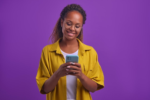 Jeune femme afro-américaine tenant un téléphone et bavardant se tient dans un studio lilas