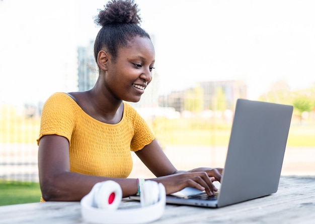 Jeune femme afro-américaine travaillant sur son ordinateur portable dans un parc de la ville étudiante préparant un examen concept de travail étudiant blogueur et influenceur à distance