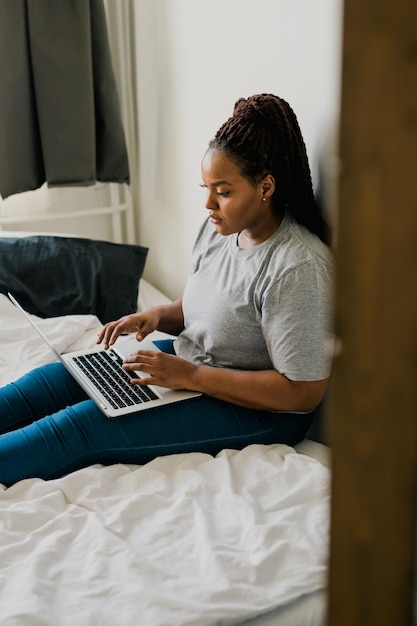 Jeune femme afro-américaine utilisant un ordinateur portable sur les technologies du lit et la communication et le réseau social