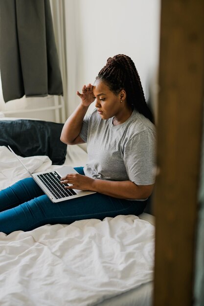 Jeune femme afro-américaine utilisant un ordinateur portable sur les technologies du lit et la communication et le réseau social