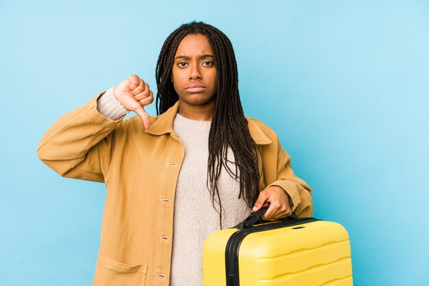 Jeune femme afro-américaine de voyageur tenant une valise isolée montrant un geste d'aversion, les pouces vers le bas. Concept de désaccord.