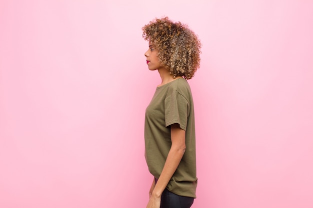 Jeune femme afro-américaine sur la vue de profil à la recherche de copier l'espace à venir, penser, imaginer ou rêver contre le mur rose