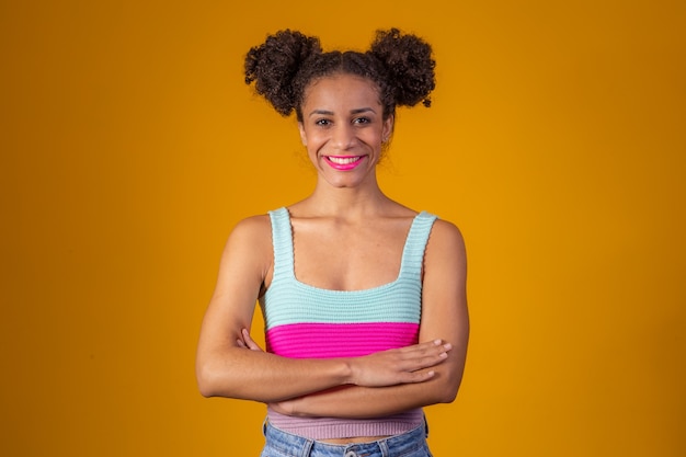 Jeune femme afro avec les bras croisés sur fond jaune avec un chignon dans les cheveux.