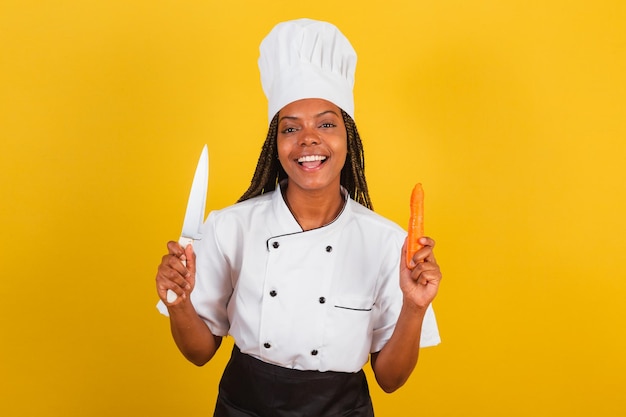 Jeune femme afro-brésilienne chef cuisinier tenant un couteau et une carotte pour éplucher et hacher