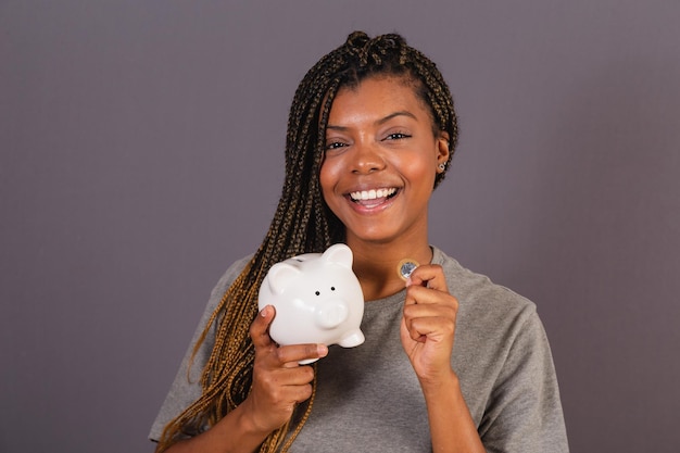 Jeune femme afro-brésilienne tenant une tirelire et un concept de pièce de monnaie d'économie finance épargne