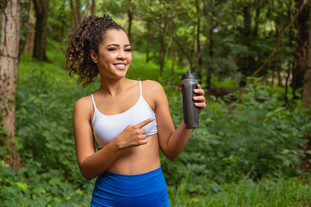 Jeune femme afro dans le parc tenant une bouteille d'eau.