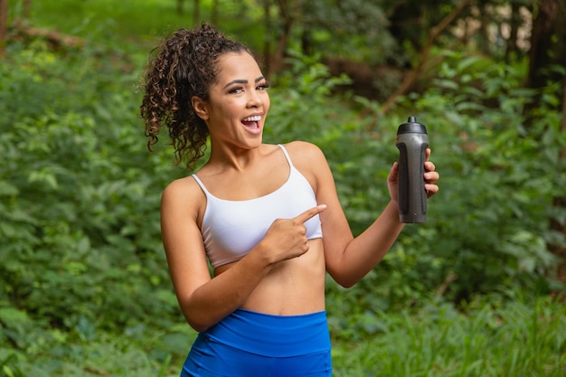 Jeune femme afro dans le parc tenant une bouteille d'eau.