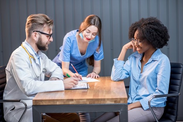 Jeune femme afro-ethnique ayant une consultation médicale assise avec un médecin et une infirmière au bureau