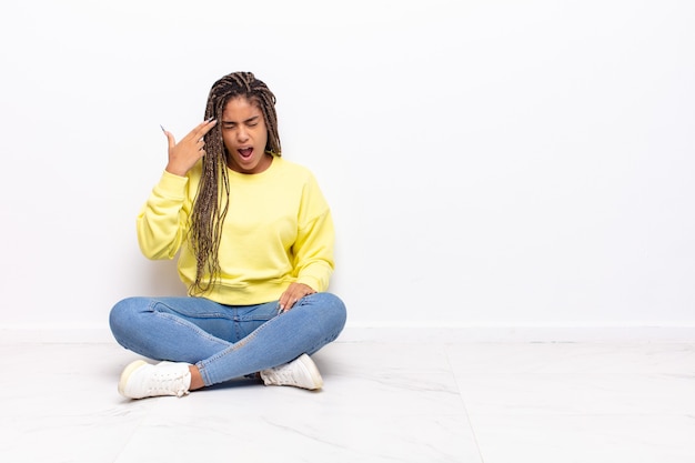 Jeune femme afro à la malheureuse et stressée, geste de suicide faisant signe des armes à feu avec la main, pointant vers la tête