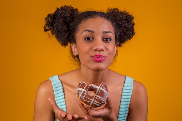 Jeune femme afro mangeant de délicieux beignets au chocolat.