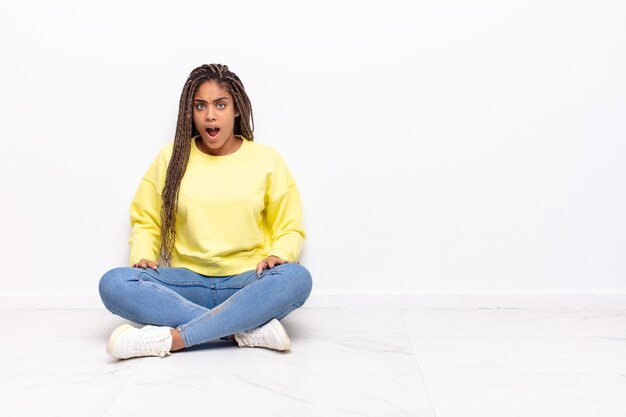 Jeune femme afro se sentant terrifiée et choquée, avec la bouche grande ouverte de surprise