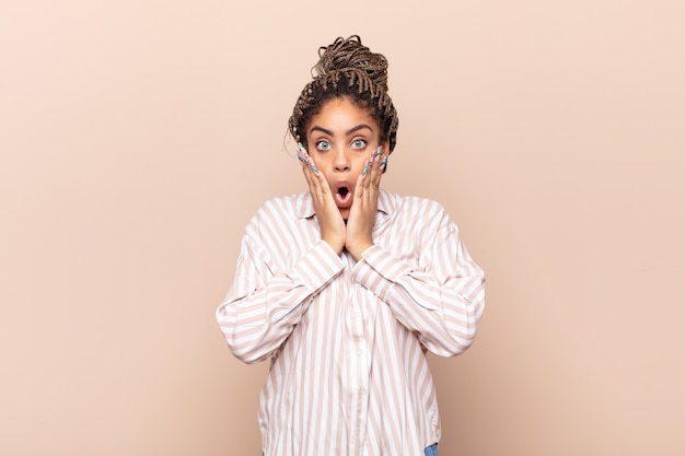 Photo jeune femme afro se sentir choquée et effrayée, à la terrifiée avec la bouche ouverte et les mains sur les joues