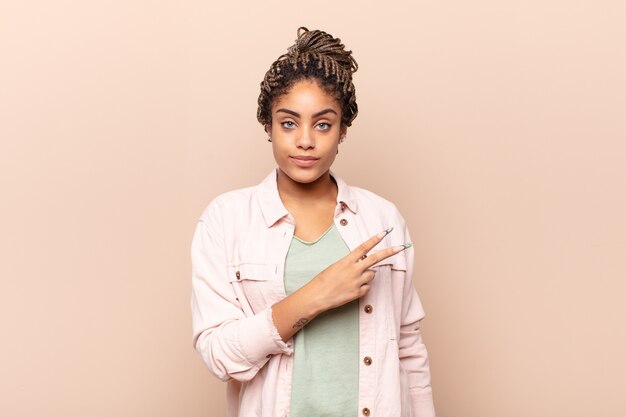 Photo jeune femme afro se sentir heureuse, positive et réussie, avec la main en forme de v sur la poitrine, montrant la victoire ou la paix