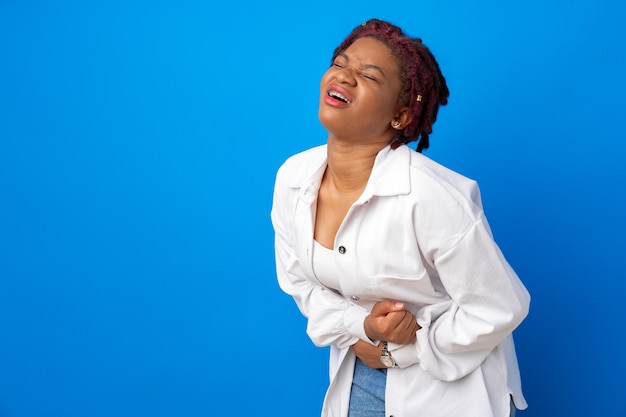 Jeune femme afro souffrant de maux d'estomac contre la surface bleue