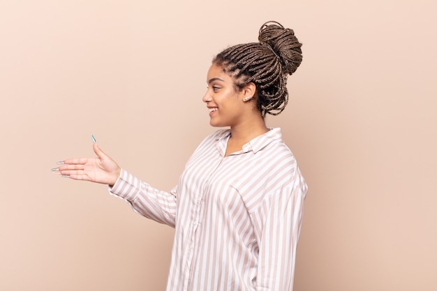 Jeune femme afro souriante, vous saluant et vous offrant une poignée de main pour conclure une affaire réussie