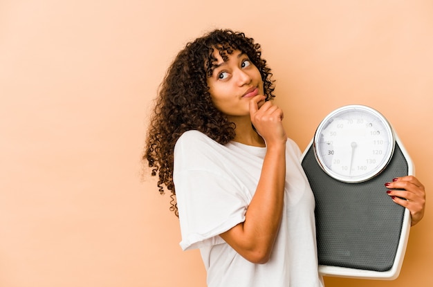 Jeune femme afro tenant une échelle à la recherche de côté avec une expression douteuse et sceptique