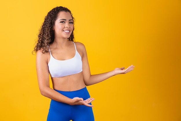 Jeune femme afro en tenue de gym pointant vers le côté avec un espace pour le texte.