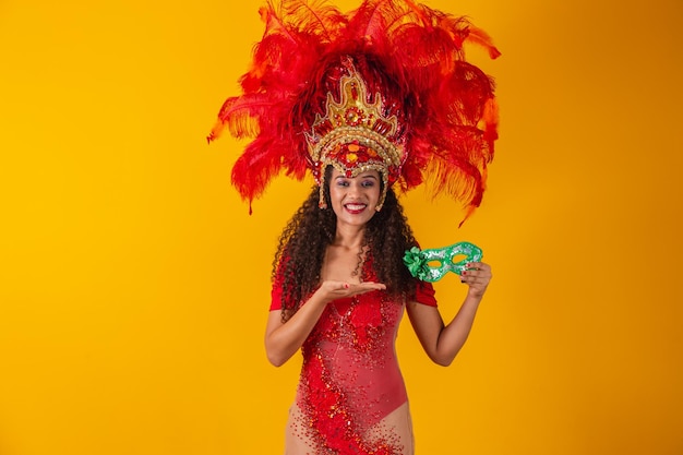 Jeune femme afro en tenue de samba et de carnaval tenant un masque vert souriant à la caméra.