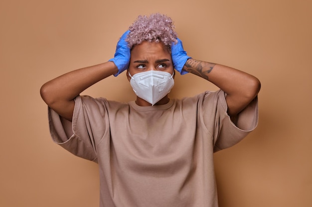 Une jeune femme agacée et perturbée a attrapé la tête avec les mains portant un masque facial et des gants en caoutchouc se sentant malade et inquiète de l'épidémie épidémique Une femme anxieuse touchant la tête avec le stress se sentant déprimée