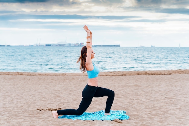 Jeune femme d'âge moyen de profil effectuant des asanas sur un tapis sur la plage. concept yoga, méditation