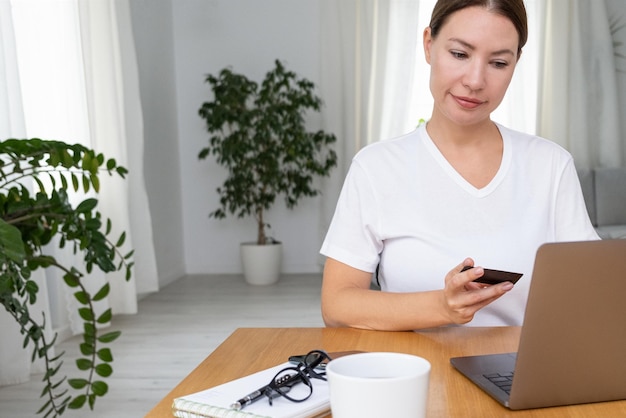 Jeune ou femme d'âge moyen vraie femme tenant une carte de crédit pour le paiement en ligne Concept de travail à distance et travaillant à domicilexA