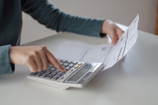 Jeune femme à l'aide de la calculatrice pour l'analyse et le calcul des factures de coûts de budget familial sur le bureau dans le bureau à domicile