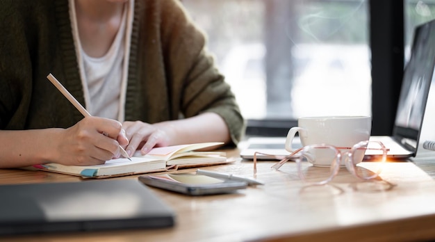 Jeune femme à l'aide d'un crayon écrit une note alors qu'elle était assise à son bureau à domicile