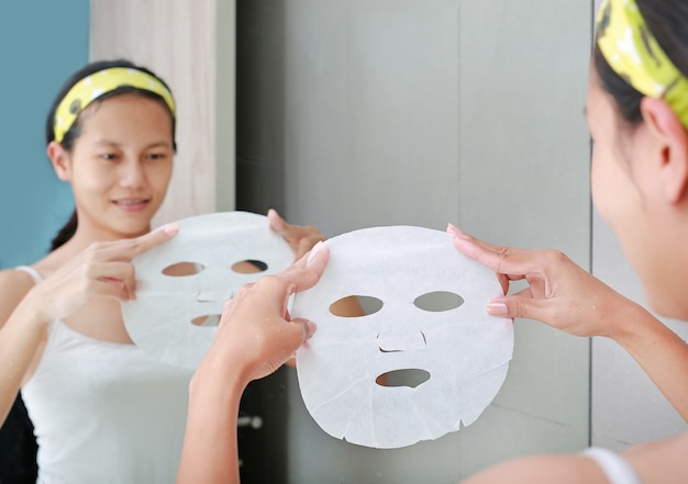 Jeune femme à l&#39;aide de masque facial cosmétique dans la salle de bain.