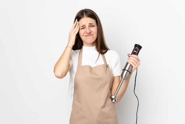 Jeune femme à l'aide d'un mélangeur à main sur un mur blanc malheureux et frustré par quelque chose.