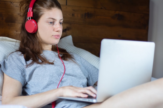 Jeune femme à l&#39;aide d&#39;un ordinateur portable et des écouteurs au lit.