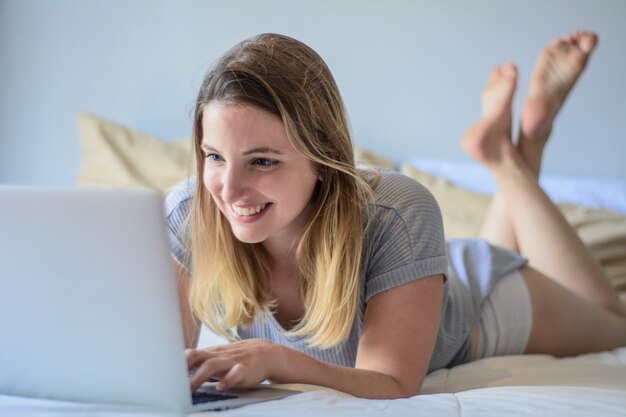 Jeune femme à l'aide de son ordinateur portable sur le lit