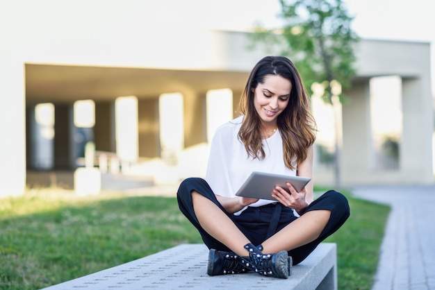 Jeune femme à l'aide de tablette numérique, assis à l'extérieur en contexte urbain.