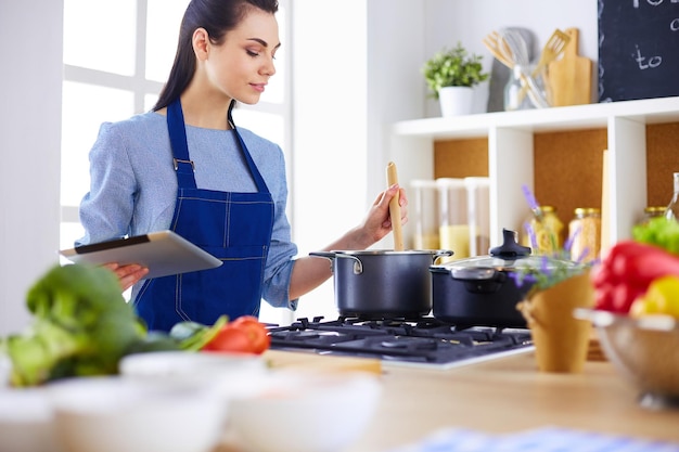 Jeune femme à l&#39;aide d&#39;une tablette PC pour cuisiner dans sa cuisine