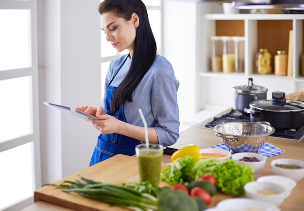 Jeune femme à l&#39;aide d&#39;une tablette PC pour cuisiner dans sa cuisine