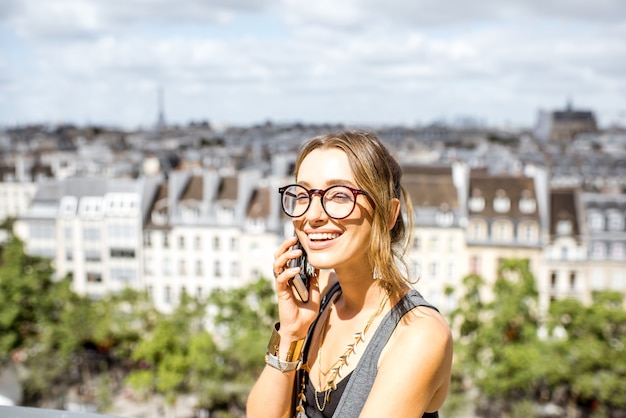 Jeune femme à l'aide d'un téléphone intelligent debout sur la terrasse avec vue imprenable sur Paris