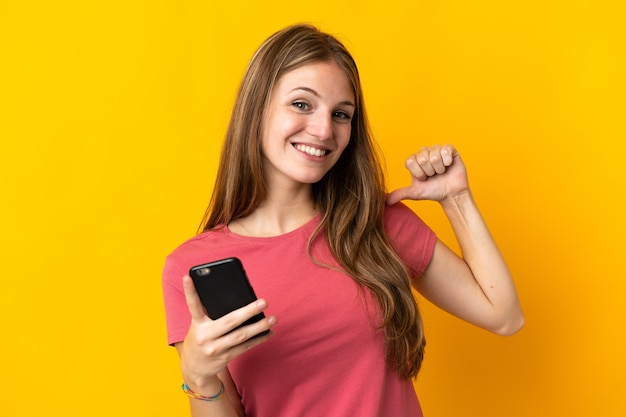 Jeune femme à l'aide de téléphone mobile isolé sur jaune fier et satisfait de soi