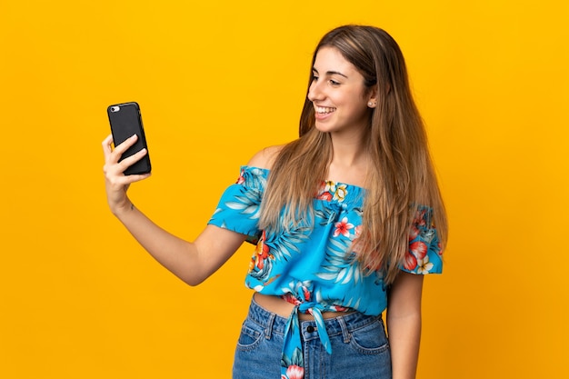 Jeune femme à l'aide de téléphone mobile isolé sur un mur jaune avec une expression heureuse