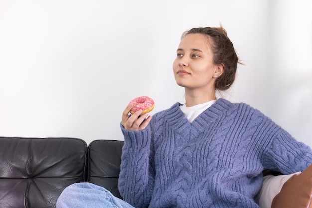 Une jeune femme aime manger un délicieux beignet appétissant sur le canapé