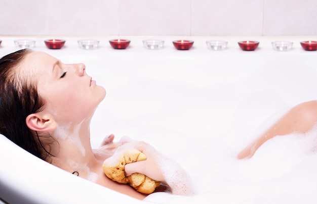 Jeune femme aime la mousse de bain dans la baignoire.