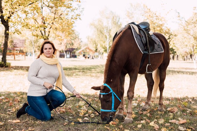 Jeune femme alimentation cheval brun en automne parc