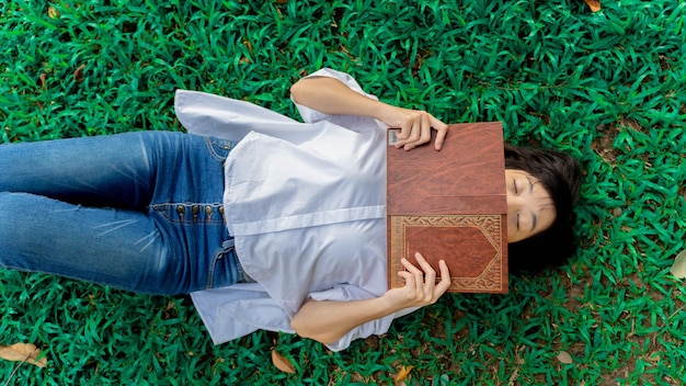 Jeune femme allongée sur l'herbe et se détendre en lisant un livre