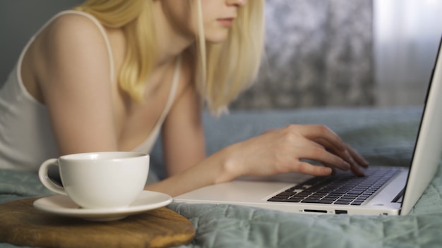 Jeune femme allongée sur le lit à l'aide d'un ordinateur portable et en tapant