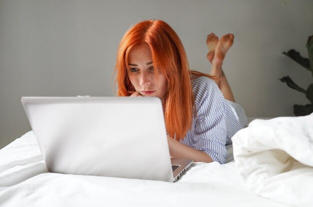 une jeune femme allongée sur un lit avec un ordinateur portable