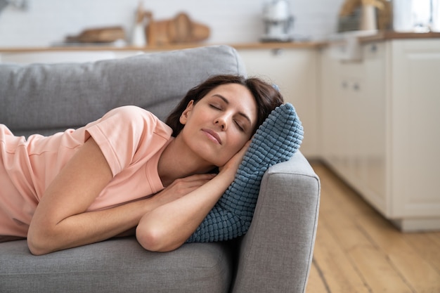 Jeune femme allongée sur l'oreiller sur le canapé, se reposer, se détendre, dormir après avoir terminé le travail de la maison